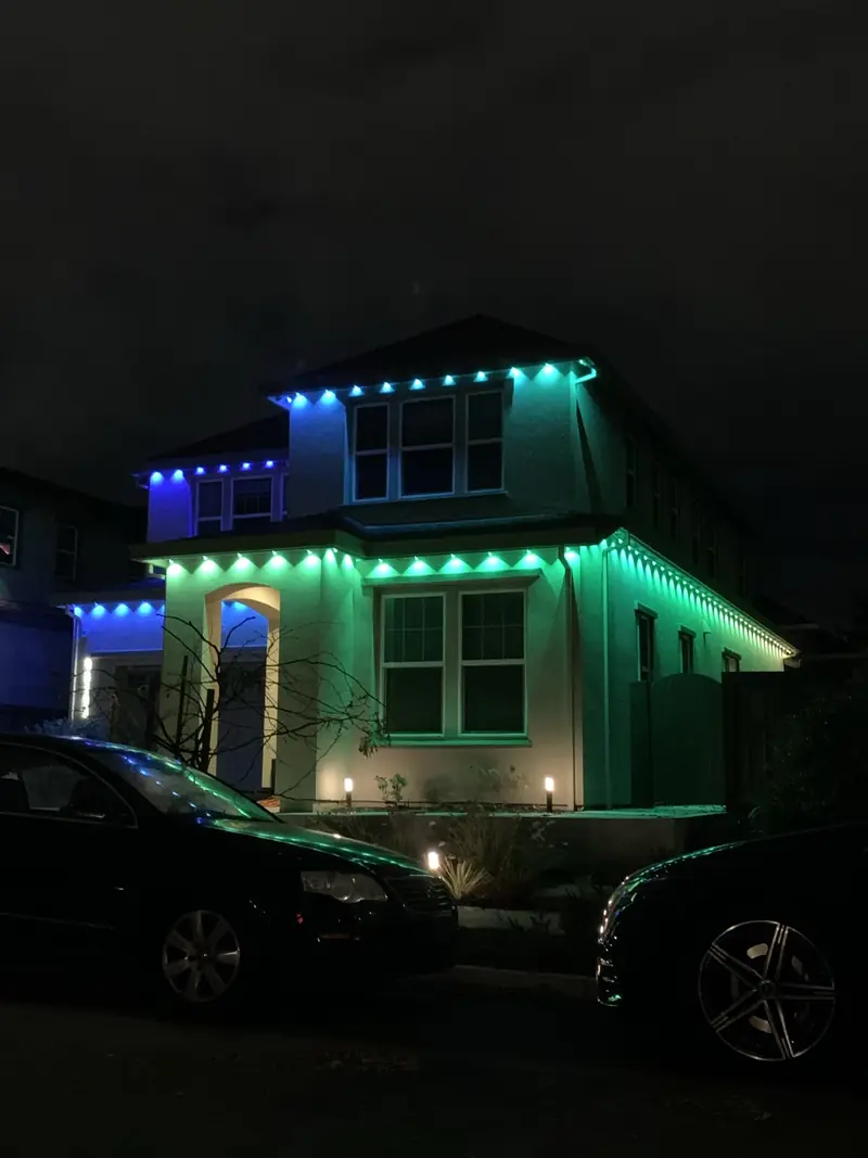 Two-story home with green and blue permanent lights along the roofline at night